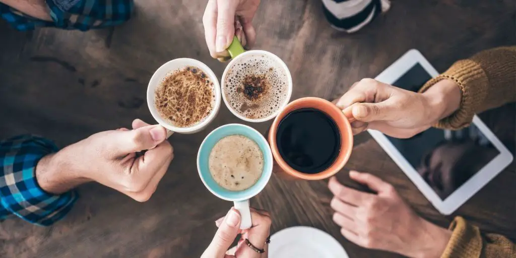 People holding up coffee mugs to cheers. Consider the number of coffee drinkers before buying a coffee maker.