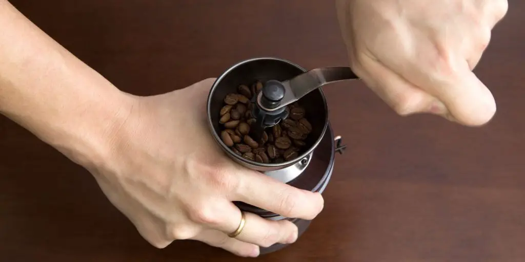 image of person using a manual coffee grinder. Using freshly ground coffee is key to fresh tasting cofee.