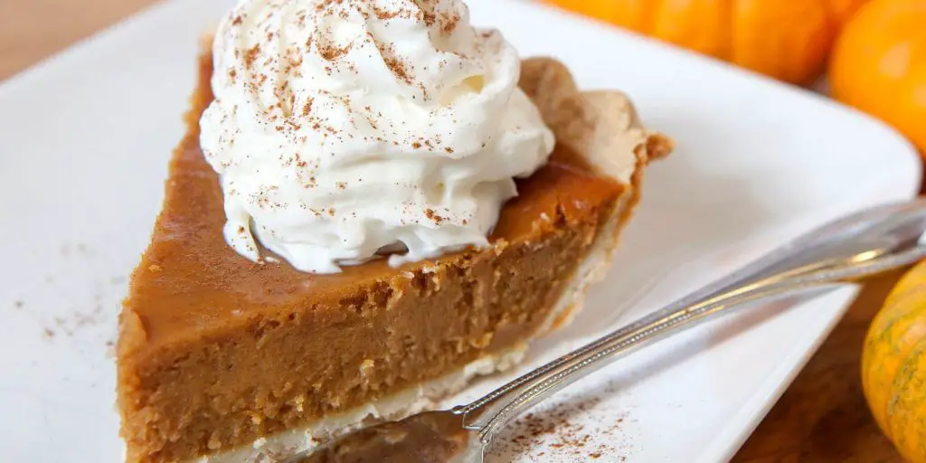 close up of a slice of pumpkin pie with whipped cream on top.