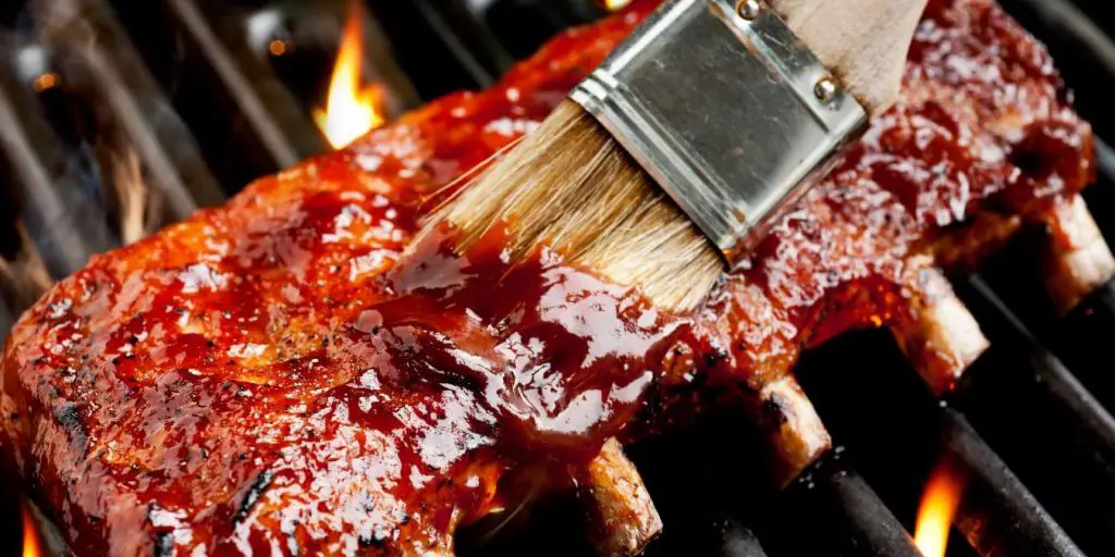ribs being basted over a barbeque fire.